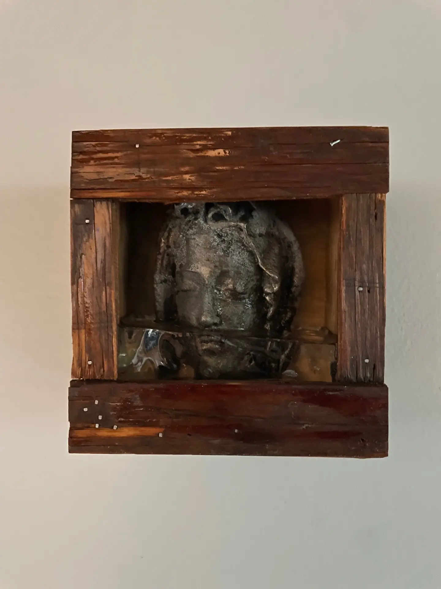 Wooden-framed sculpture of a serene women's face with implied water up to but not covering her nose.