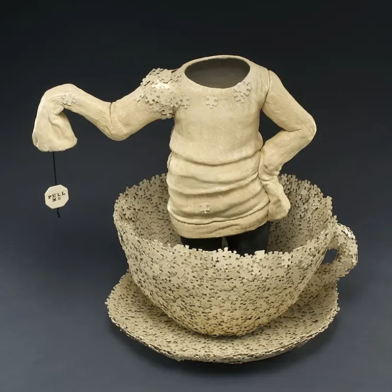 Ceramic Sculpture of empty children's clothing emerging from teacup puzzle sculpture